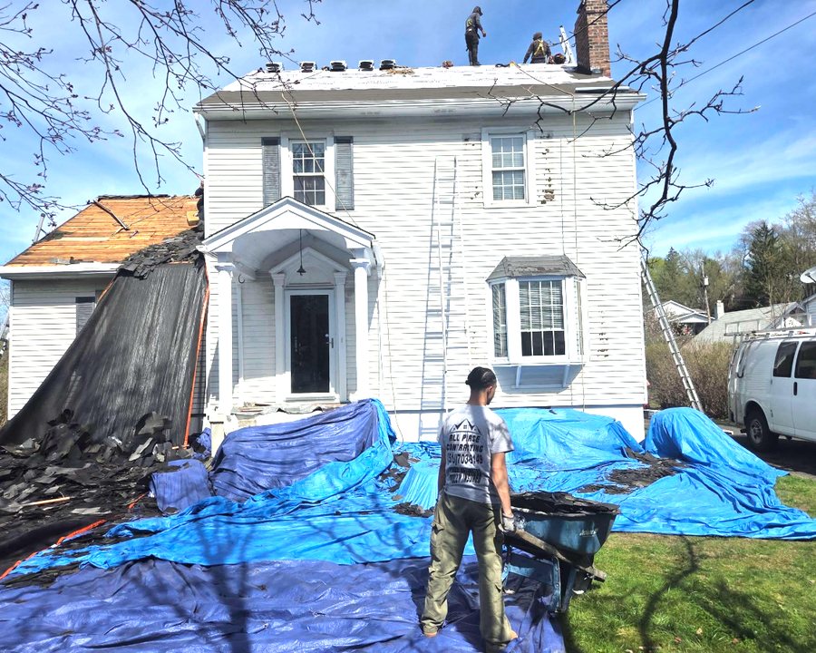 All Phase Contracting crew tearing off an old roof, debris tarped off the lawn