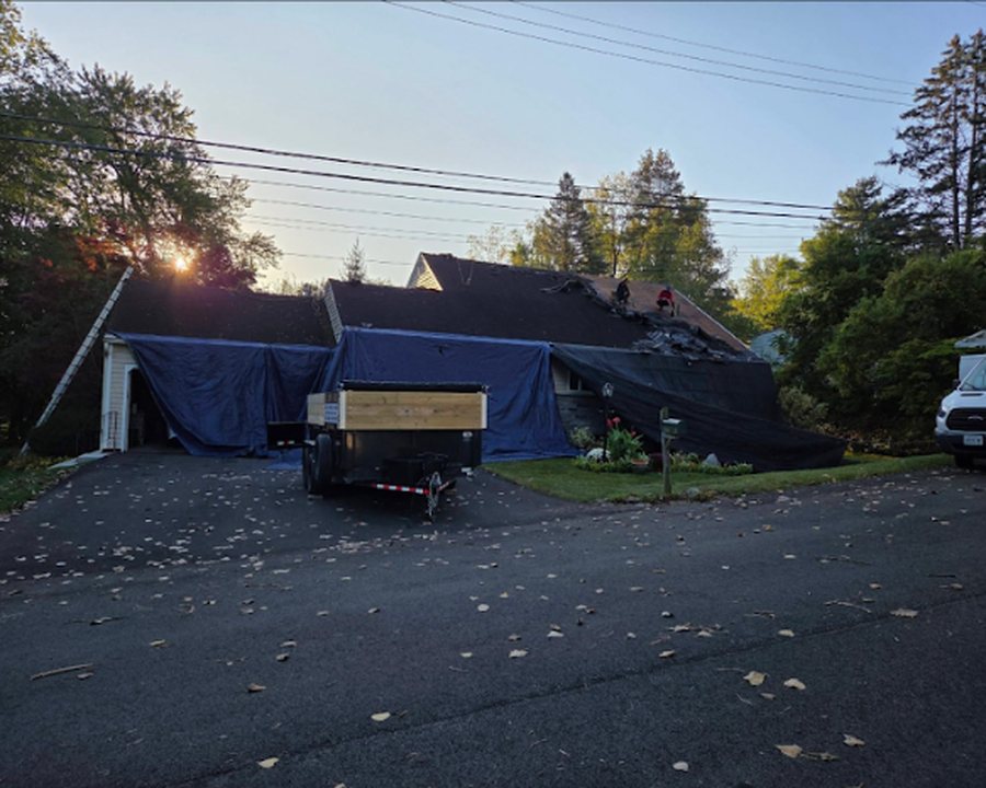 Tear-off and re-roof in progress with the home tarped and dump trailer on site